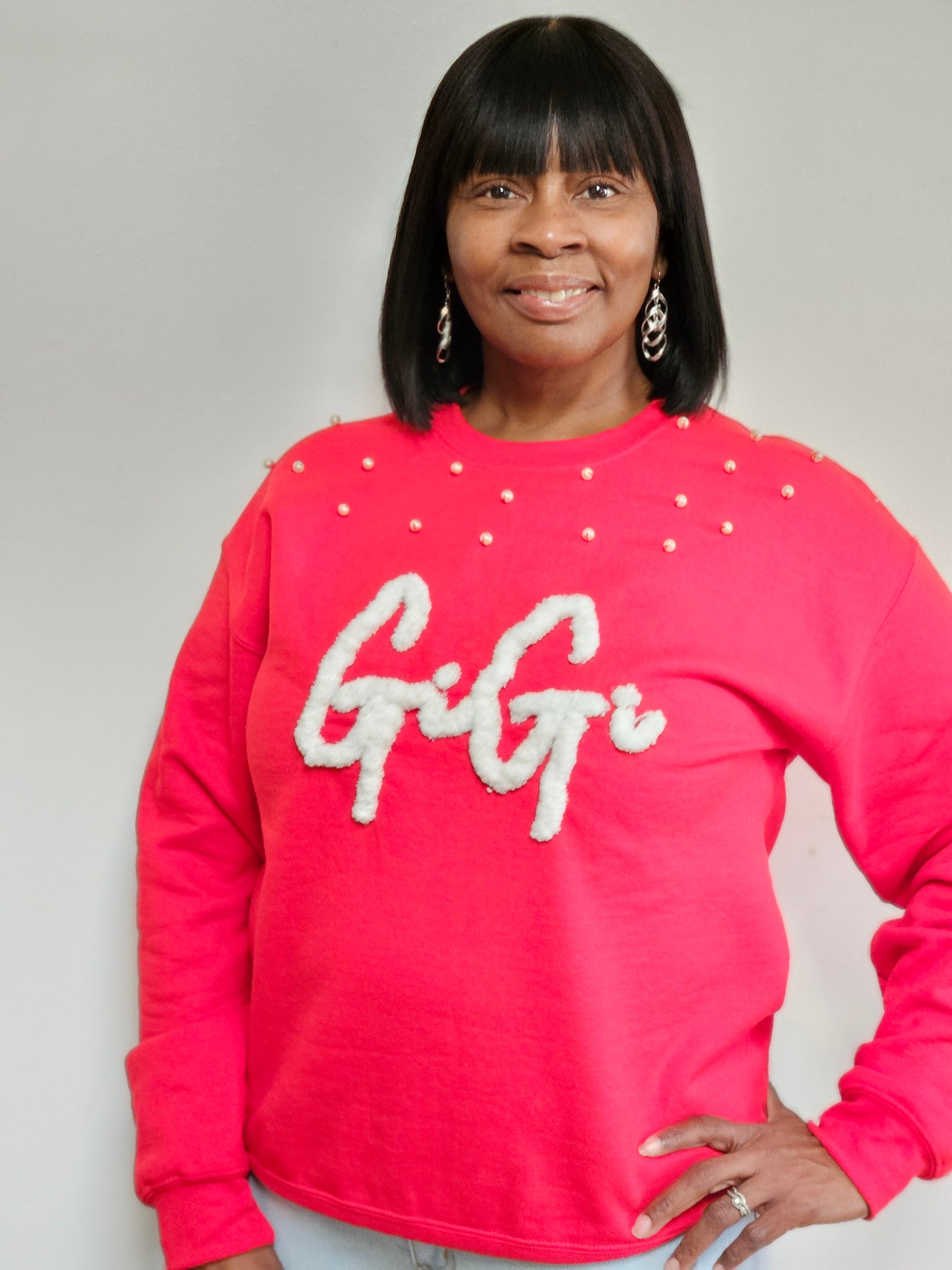 Woman wearing a red sweatshirt with 'Gigi' on it against a gray background